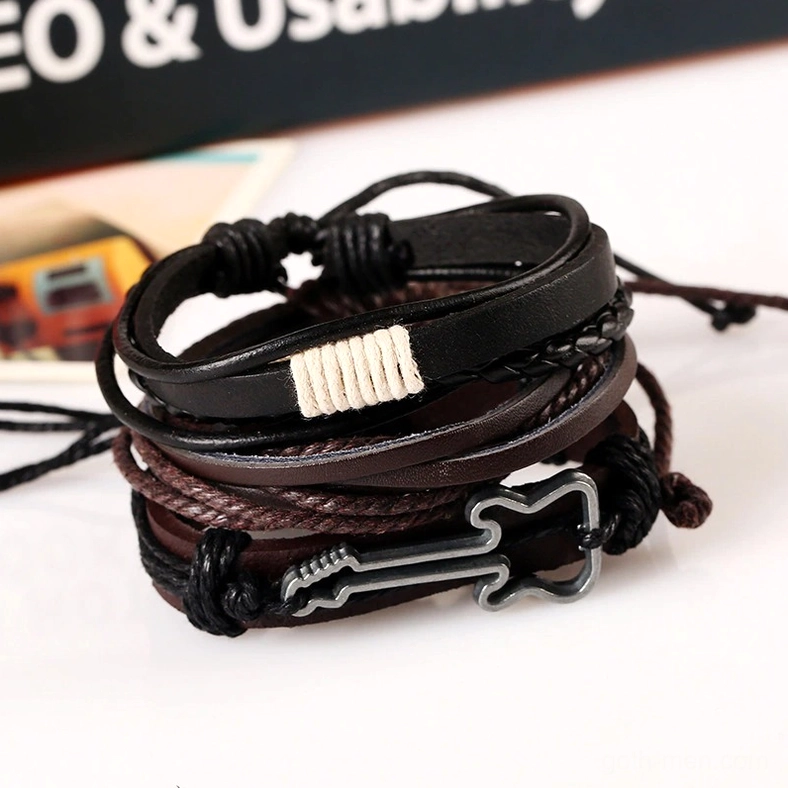 Multi-layer vintage gothic leather bracelet featuring woven fabric detail, guitar metal charm pendant, mixed leather layers in brown and black tones, displayed in flat lay against book background