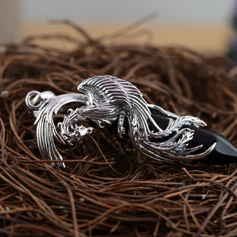 Black obsidian phoenix sterling silver pendant top-down view on textured natural straw background, showing detailed metalwork