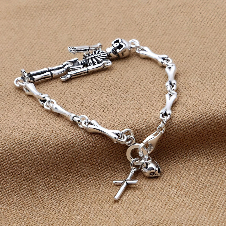 Vintage skeleton silver bracelet with cross charm displayed on neutral fabric, showing bone chain links and toggle fastening