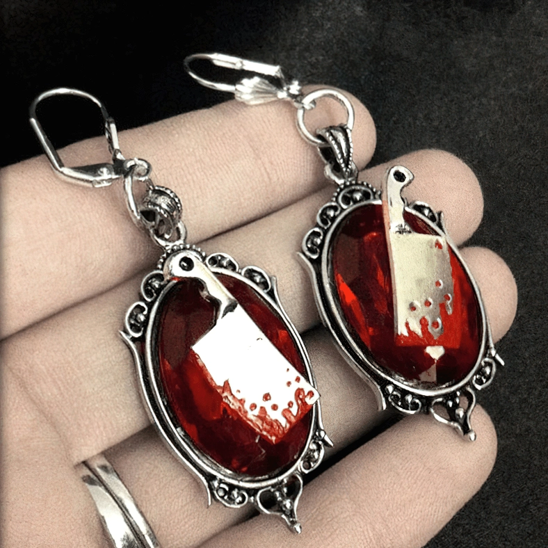 Red meat cleaver gothic earrings held in hand showing blood-splattered silver cleaver design and resin gem close-up