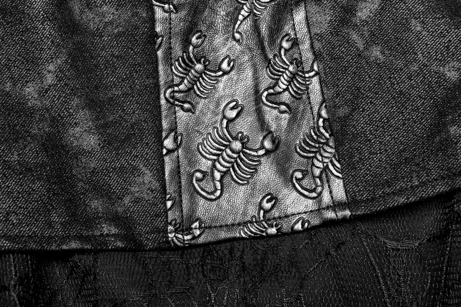 Close-up of scorpion embossed silver patch on gothic coat fabric with worn texture