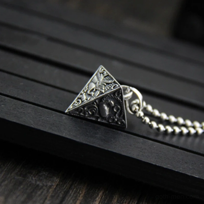 Rear angled view of oxidized silver pyramid pendant with embossed carvings and decorative details on slatted wooden surface