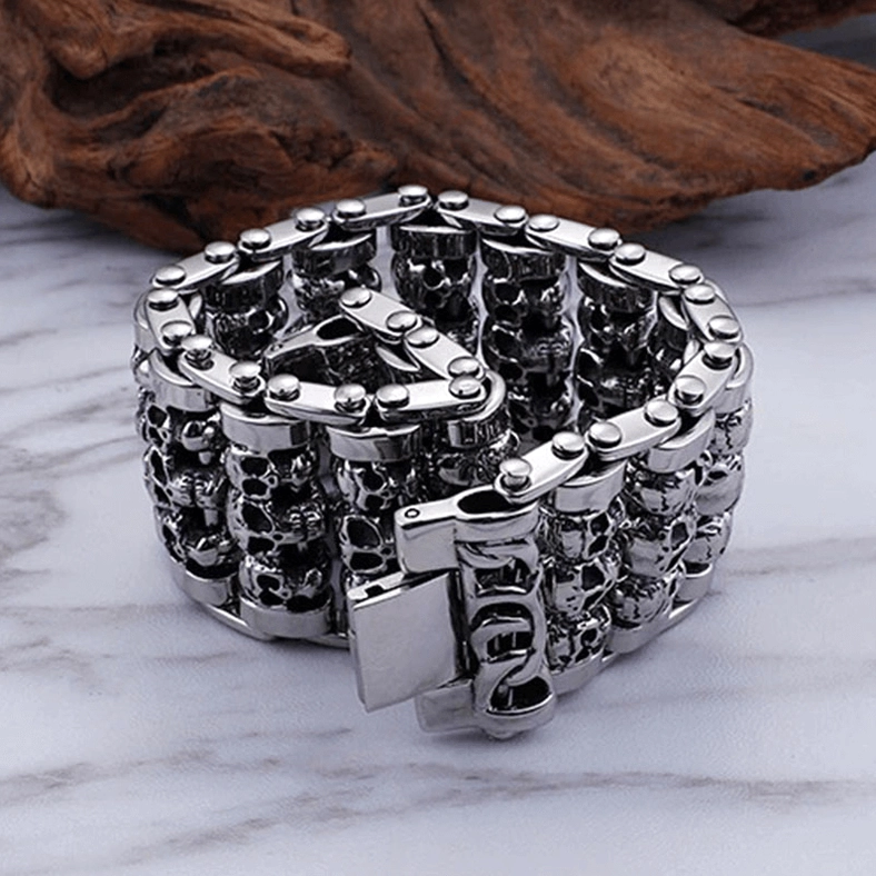 Silver gothic skull chain bracelet with fold-over clasp on marble and wood texture background