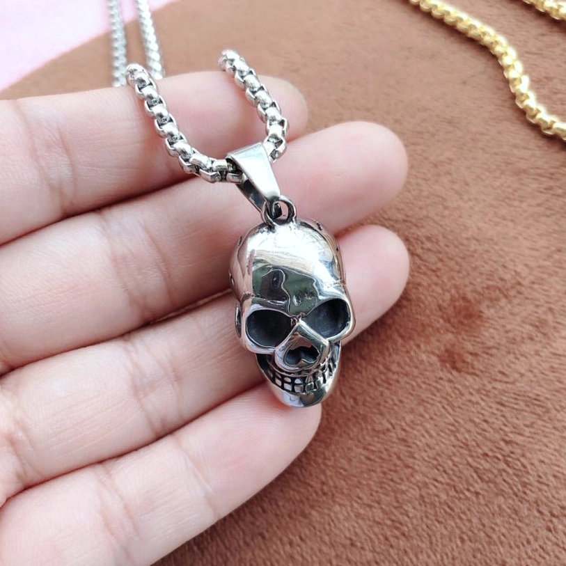 Silver skull pendant necklace worn on hand side angle, showcasing polished stainless steel finish