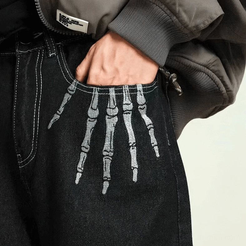 Skeleton finger hand embroidery detail on gothic jeans pocket, studio close-up view