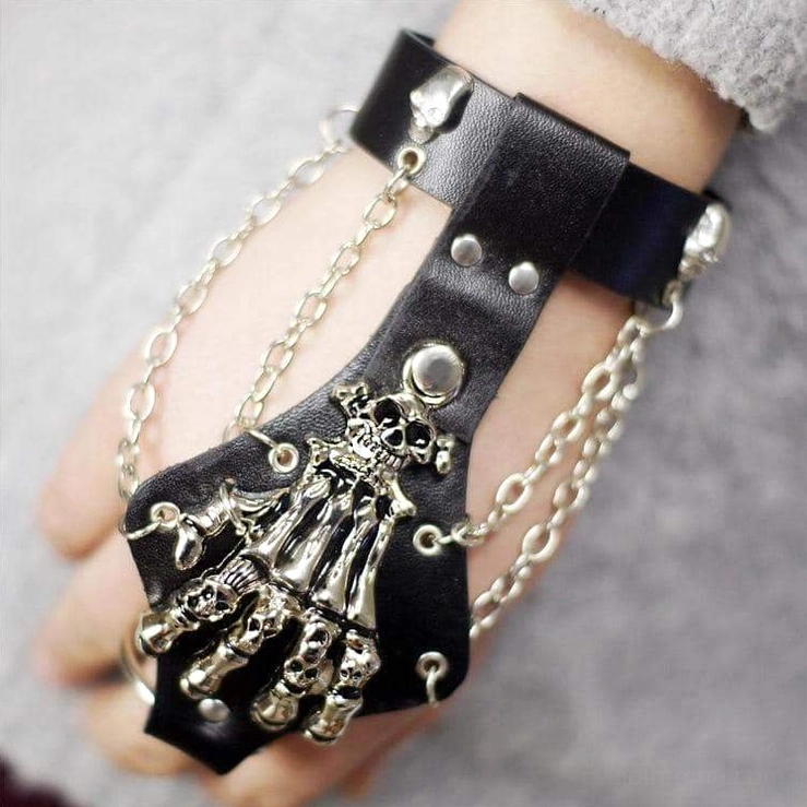 Close-up wearable view of gothic skeleton hand chain leather wristband on human wrist, showing chain tassels and finger positioning