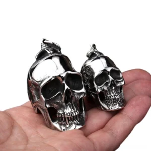 Dual-size stainless steel skull pendants displayed on palm with white background showing size comparison