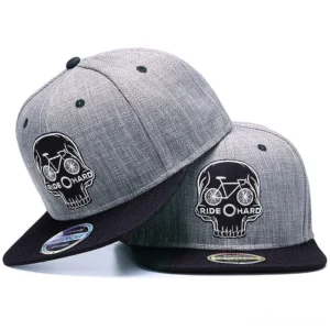 Two matching skull ride hard gothic snapback caps displayed at oblique angle, showing heather gray crown with black embroidered skull and bicycle motif