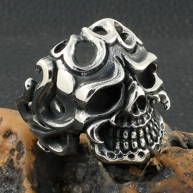 Front close-up of aged silver skull ring with black patina on rock texture background, showing intricate hollow tribal patterns and gothic details