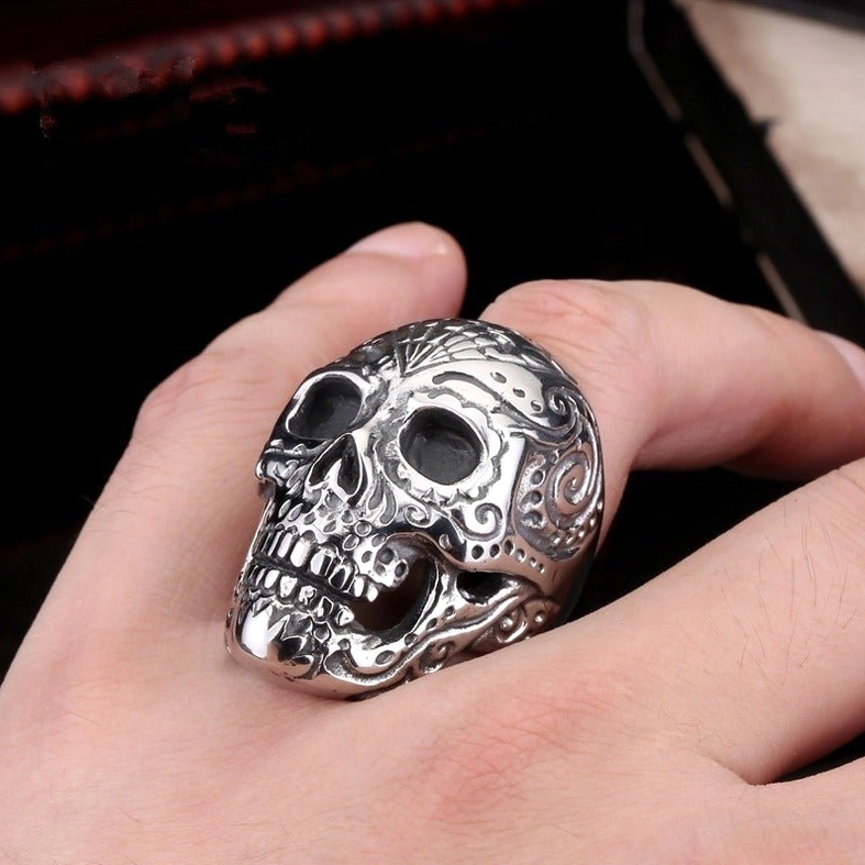 Ornate skull ring with scrollwork engravings worn on hand, side angle next to antique jewelry case, dark gothic styling
