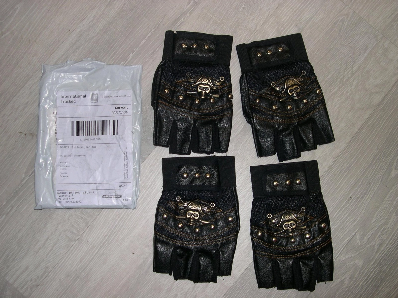 Multiple pairs of black skull studded fingerless gothic gloves displayed on wooden surface with shipping packaging