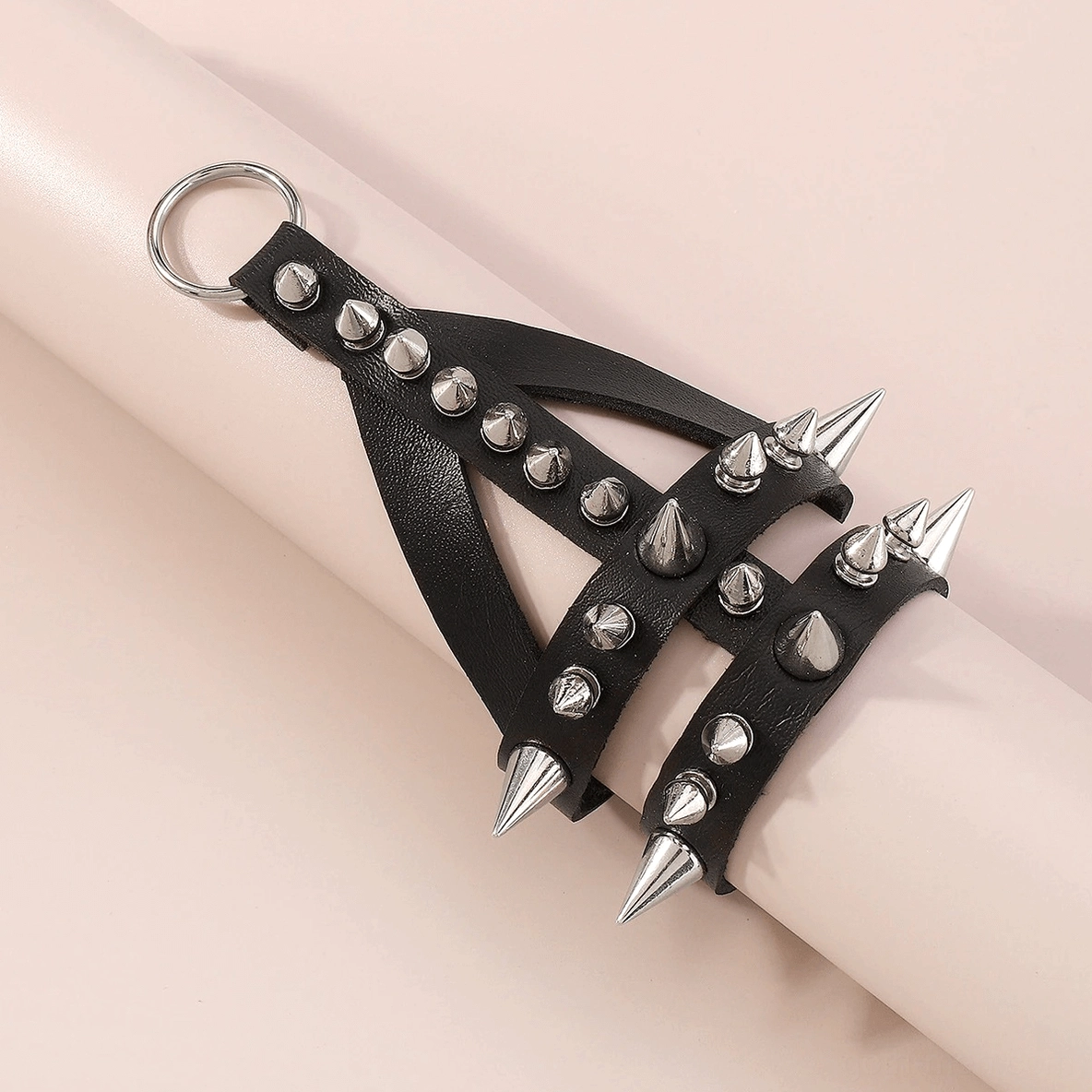 Flat lay of black leather spiked bracelet with metal D-ring on light background, showcasing all studs and details