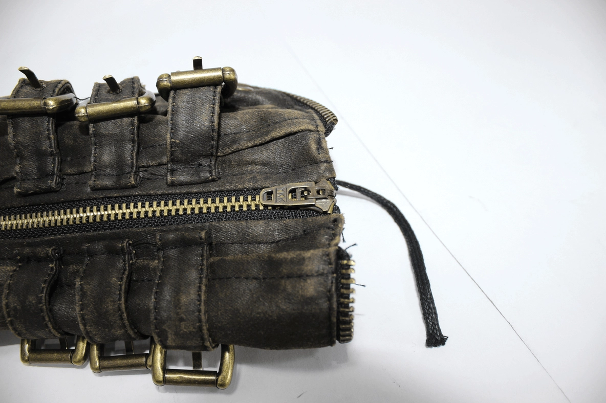 Close-up detail of brown steampunk glove featuring metal buckles, front zipper, and distressed leather texture