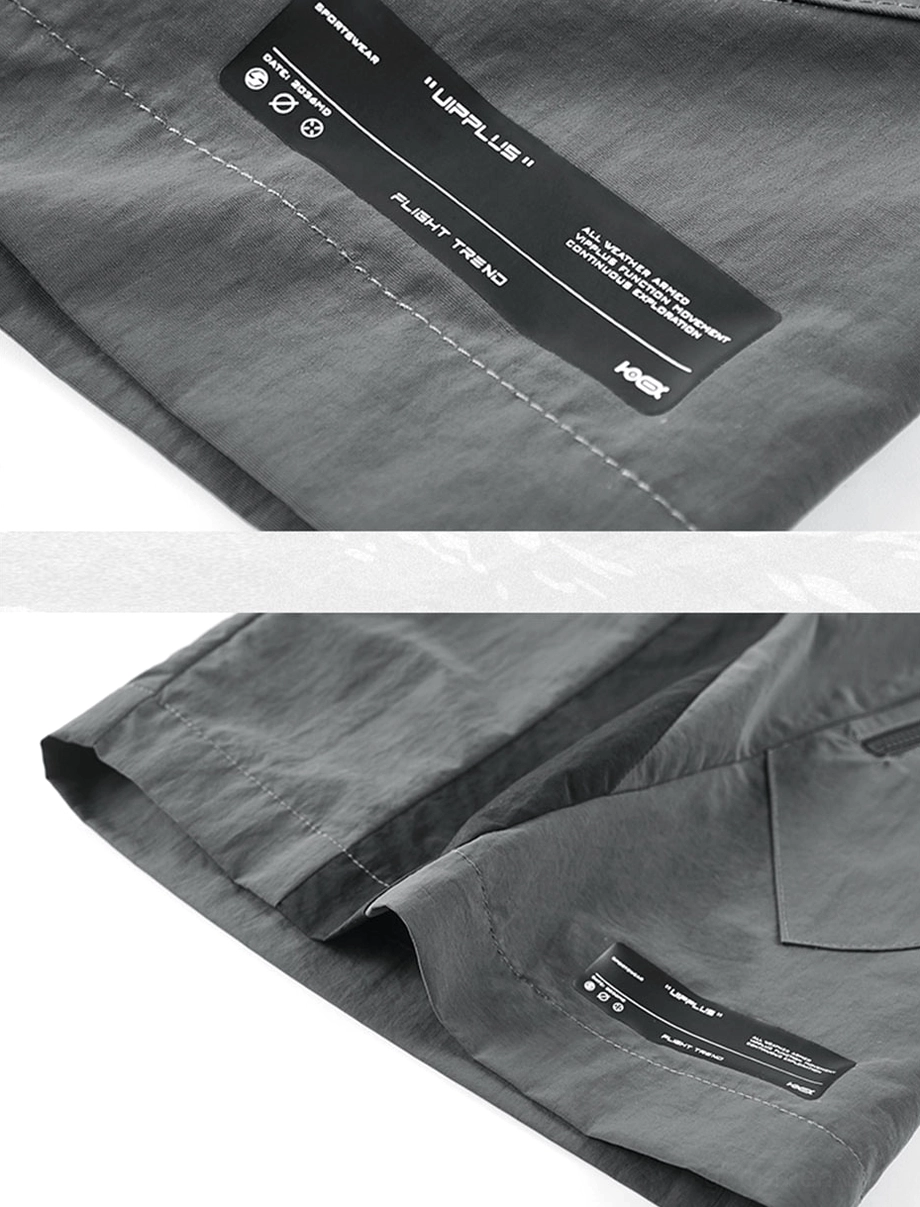Flat lay angled view of tactical cargo shorts showing size label tag, hem construction, and overall patchwork design