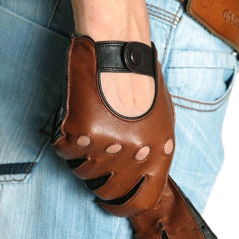 Front close-up of tan brown leather driving gloves worn with blue denim, displaying breathable cutouts and gothic hardware strap