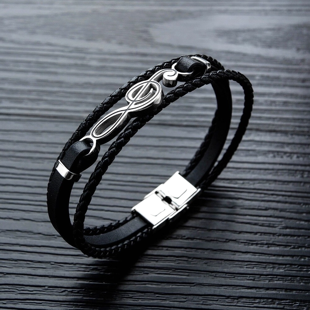 Black braided leather bracelet close-up flat lay showing stainless steel clasp fastener treble clef charm detail gothic music symbol jewelry