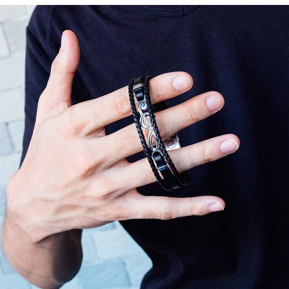 Men's treble clef leather bracelet worn on male hand front close-up view against dark casual top background gothic alternative fashion styling