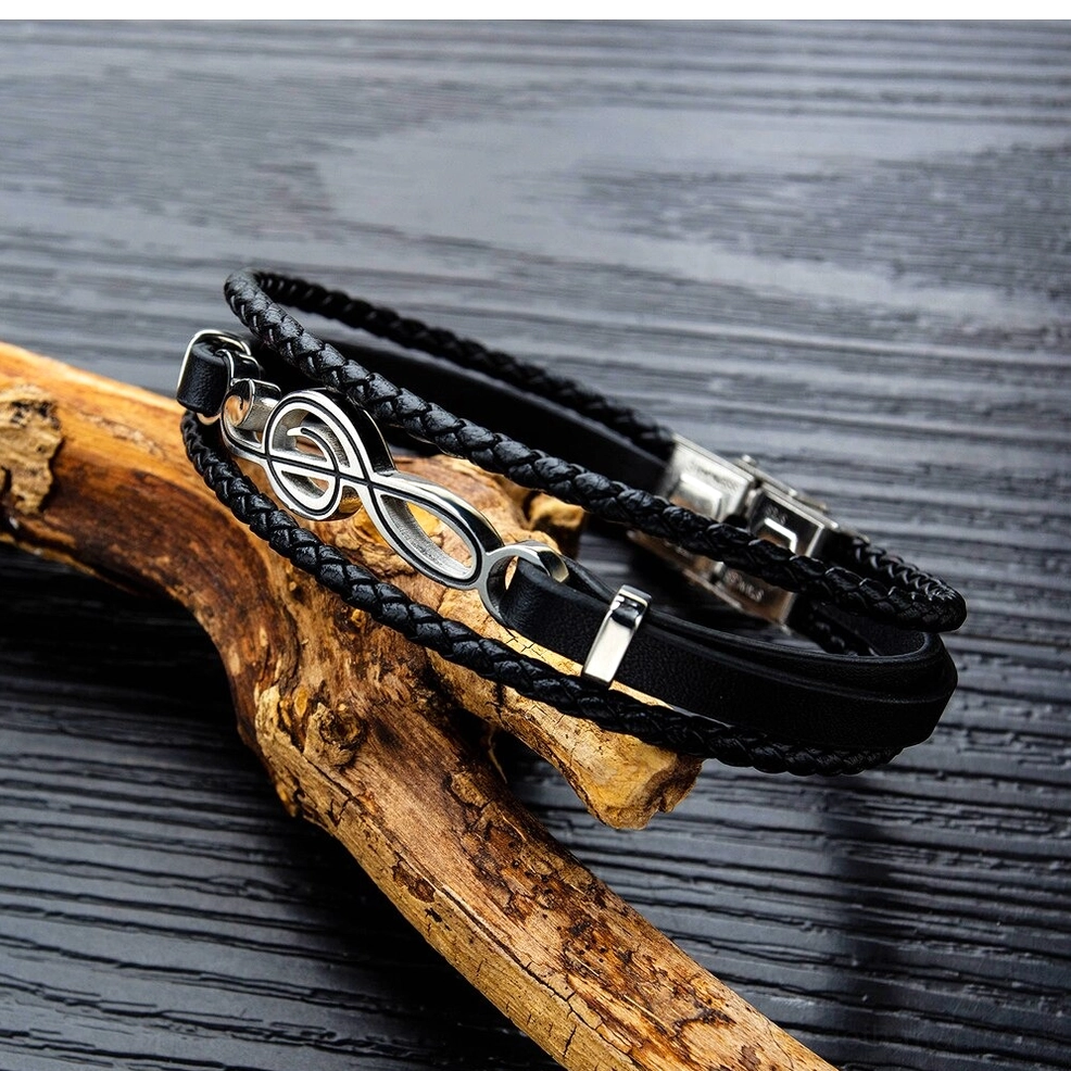Two matching treble clef leather bracelets oblique flat lay on wood driftwood background showing stainless steel music symbol accents gothic bracelet collection