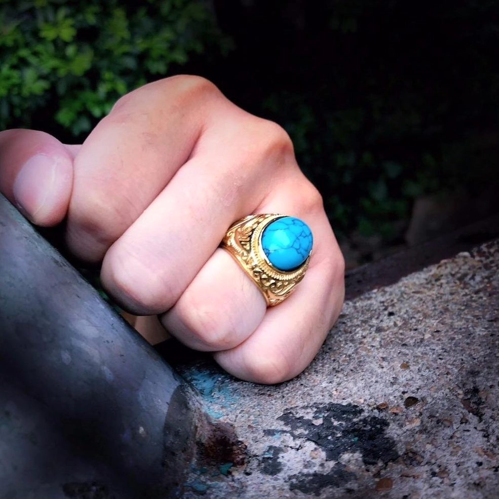 Turquoise gothic ring worn on male hand, gold tone band, alternative jewelry styling