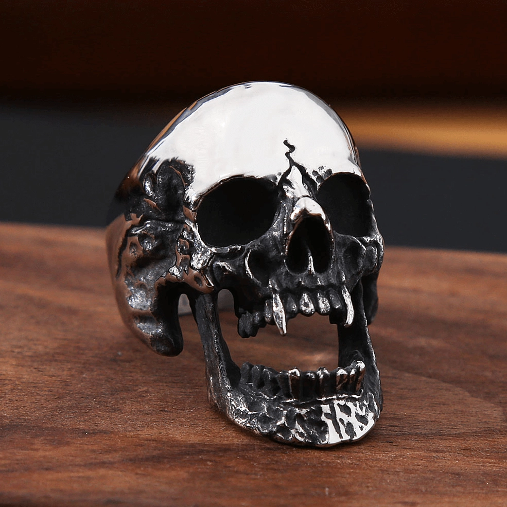 Vampire skull ring three-quarter front view showcasing distressed blackened texture and hollow open jaw design on wooden background