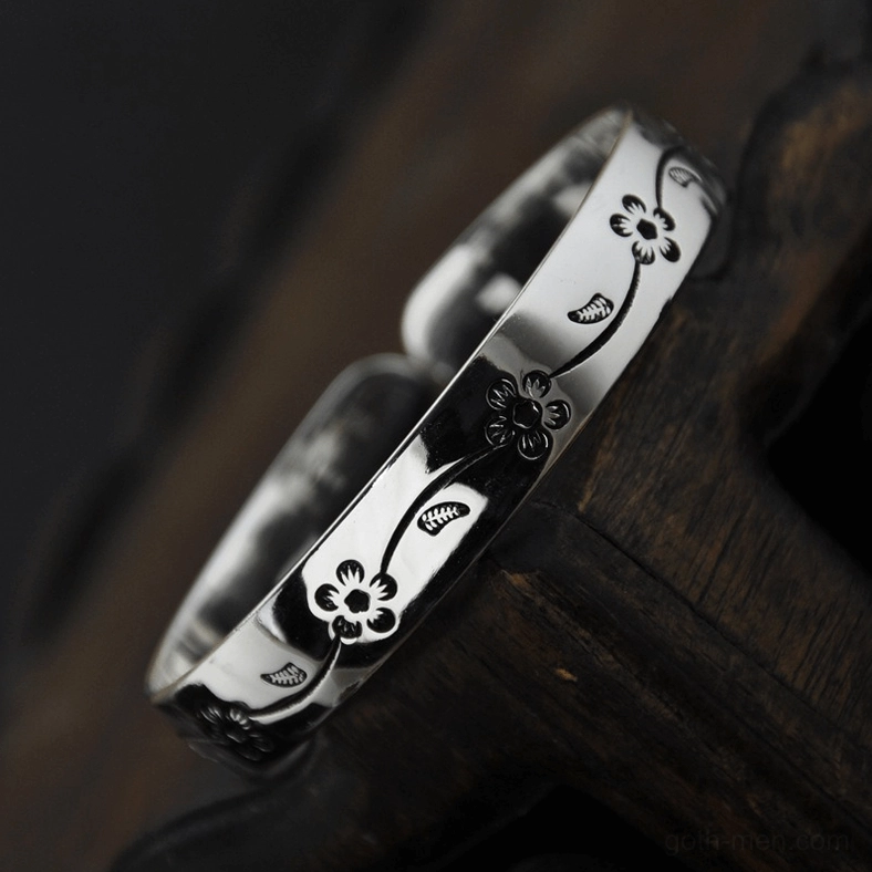 Vintage floral cuff bangle with oxidized dark engraving on retro silver finish, close-up side view on wooden background