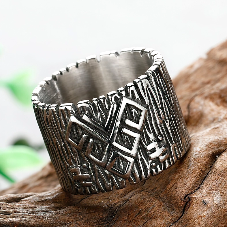 Three-quarter view of wide band rune ring with vintage silver tone and embossed rune symbols against wooden surface with green foliage
