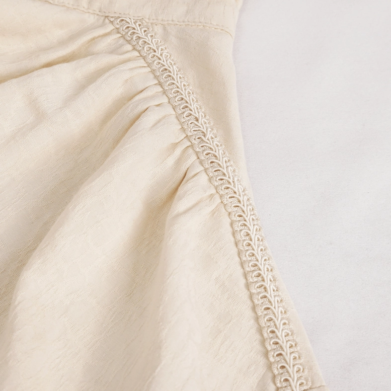 Beige cotton shirt pleated trim detail, showing embroidered decorative lace and gathered fabric folds on torso