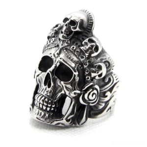 Vintage silver skull biker ring with multiple skull engravings, oblique left-side view showing aged stainless steel finish and intricate carved patterns