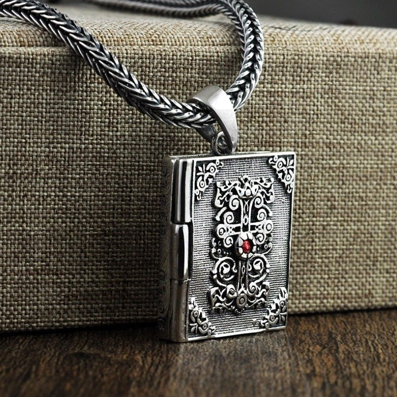 Standing sterling silver vintage bible locket pendant front view showing patinated finish and ornate religious design on fabric backdrop
