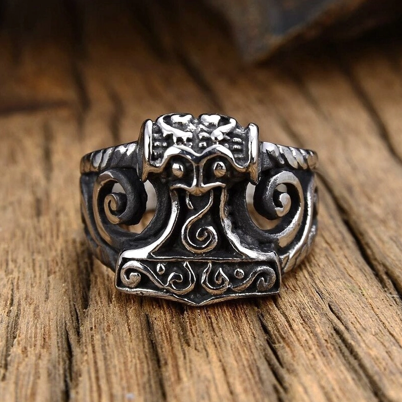 Dark aged silver Thor's Hammer gothic ring on retro wooden table background with Nordic carved scroll motifs - atmospheric styling
