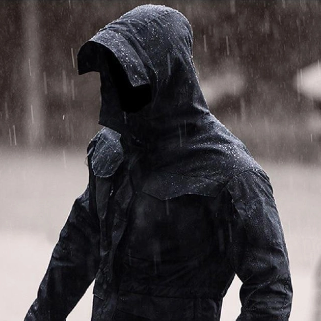 Hooded waterproof tactical jacket rear view on male model in rainy outdoor environment showing water-resistant black fabric