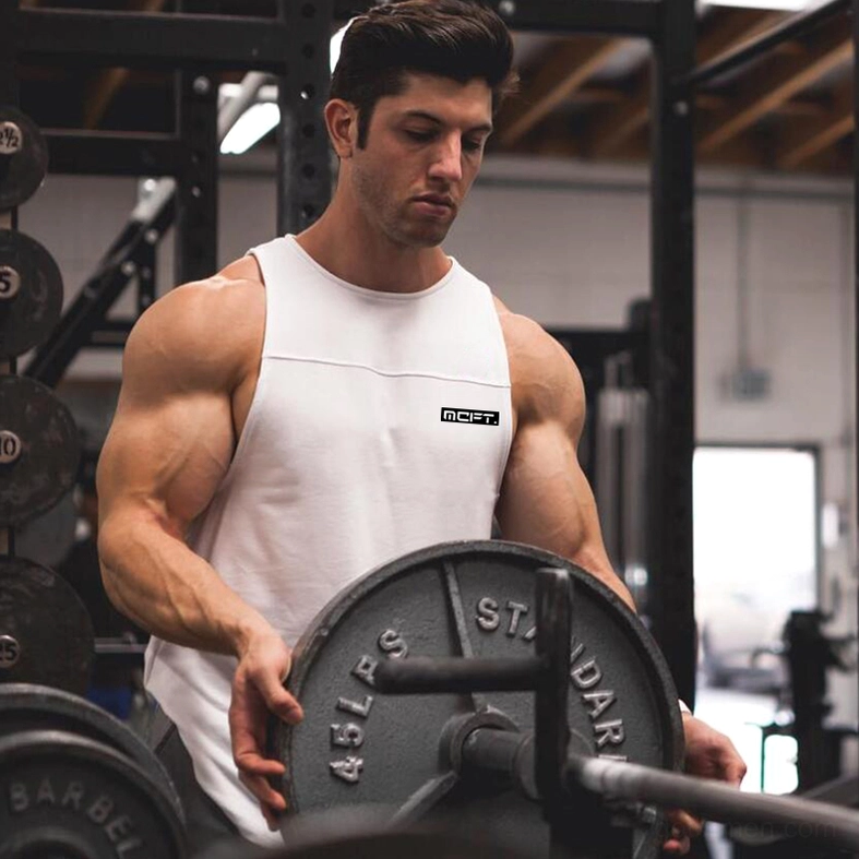 Muscular man wearing white gothic tank top lifting barbell weights in gym