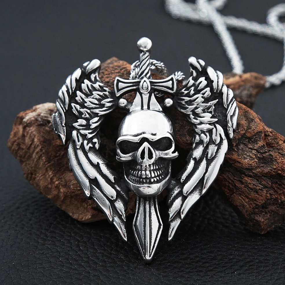 Angled front view of gothic winged skull pendant on wood leather background showing carved wing and skull details